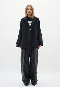 Black wool coat with a wide collar and two large buttons, layered over a black and white striped sweater. Loose-fitting black leather pants.