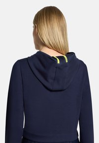 Granatowa bluza z kapturem o gładkiej teksturze z żółtymi akcentami; posiada kaptur i krótki krój. Widok od tyłu, ukazujący linię dekoltu i rękawy.