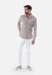 Weißes Langarmhemd mit rotem Blumenmuster, mit Knopf-down Kragen, kombiniert mit weißen Hosen und beigen Loafers. Minimalistisches Design.