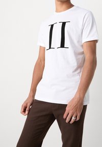 Camiseta blanca de algodón con un gráfico negro audaz "II" en el frente, cuello redondo, mangas cortas y corte relajado.