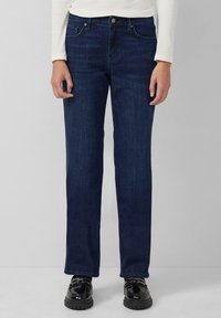 Dunkelblaue Jeans aus Denim mit einem geraden Schnitt, fünf Taschen und einem klassischen Knopfverschluss. Kombiniert mit schwarzen Schuhen.