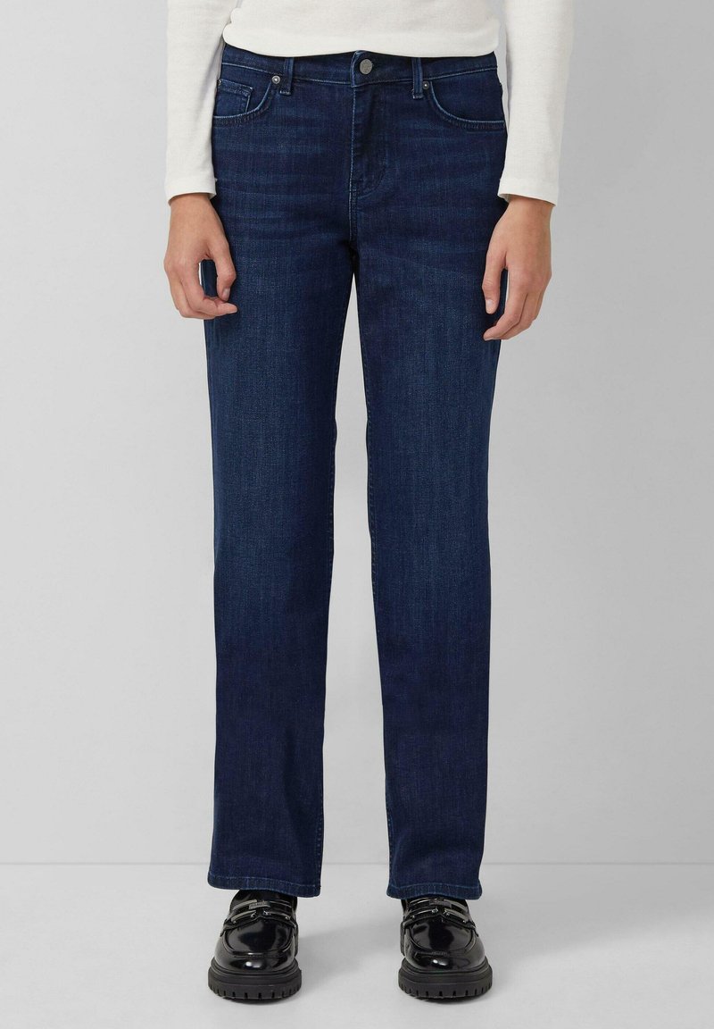 Dunkelblaue Jeans aus Denim mit einem geraden Schnitt, fünf Taschen und einem klassischen Knopfverschluss. Kombiniert mit schwarzen Schuhen.