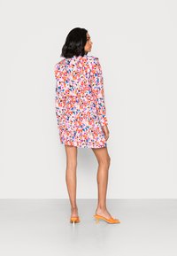 Vestido com estampa floral em cores vibrantes de rosa, laranja e azul, com mangas longas e barra em camadas de babados. Combinado com mules de salto laranja.