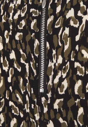 Nahaufnahme eines Stoffes mit Animal-Print in Schwarz, Weiß und Olivgrün, in dessen Mitte sich ein vertikaler silberner Metallreißverschluss befindet.