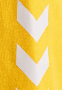 Gul textil med en strukturerad yta som har ett djärvt vitt zigzag-mönster, ordnat vertikalt och centrerat på tyget.