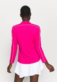 Long-sleeve pink athletic shirt with white side stripes, smooth texture, and a collar, paired with a white skirt.