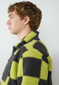 Fleece pullover in een dambordpatroon; grijs en neon groen; hoge kraag met rits; gestructureerde stof; atletische pasvorm.