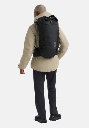 Black roll-top backpack with adjustable straps, mesh accents, and logo. Worn by a person in a beige jacket, showcasing a sleek, minimal design.