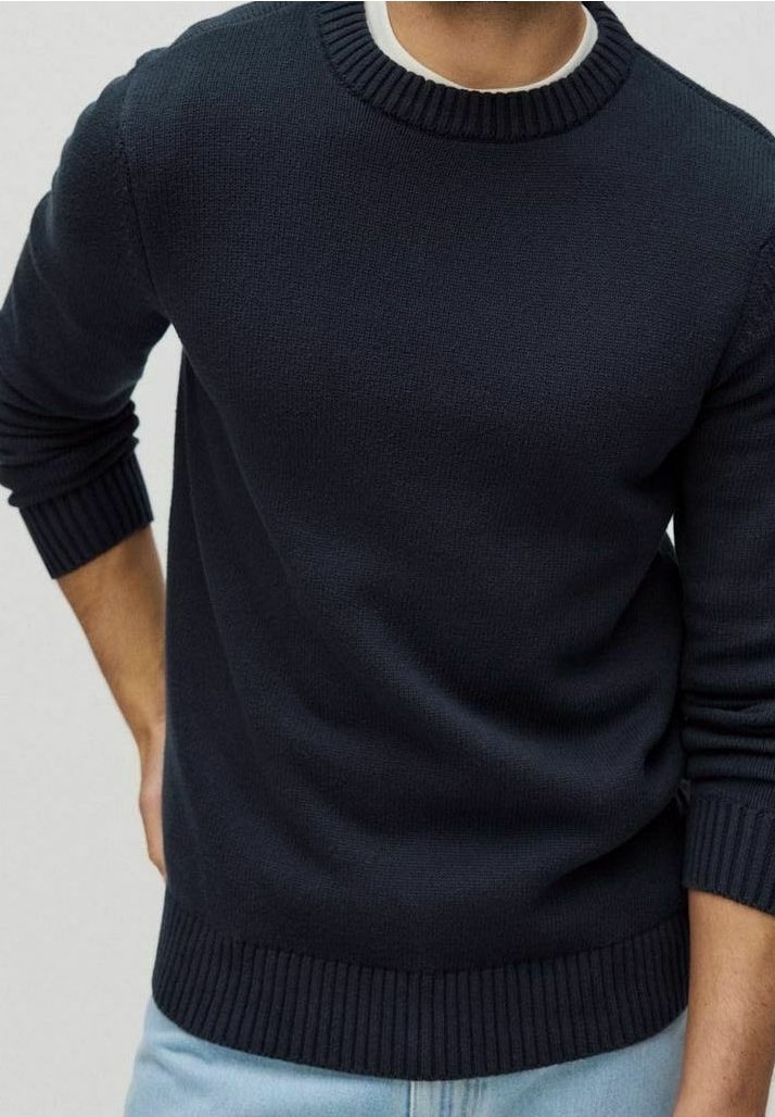 Uomo che indossa un maglione lavorato a maglia di un blu navy scuro con polsini, colletto e orlo a coste, abbinato a jeans azzurri.