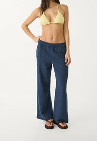 Haut de bikini jaune texturé associé à un pantalon bleu léger à jambes larges, doté d'une ceinture élastique et d'une texture de tissu douce et froissée.