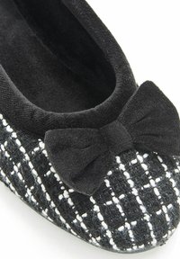 Chaussure plate noir et blanc arborant une texture tissée avec un motif en quadrillage, un doux accent de nœud noir, et une doublure intérieure moelleuse.
