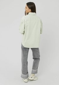 Chemise en velours côtelé vert clair avec une coupe décontractée, un devant à boutons et des manches légèrement ballonnées. Associée à un jean gris et des baskets blanches.