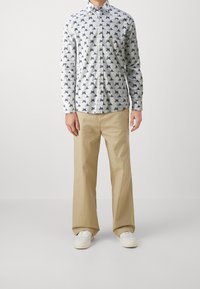 Koszula zapinana na guziki z jasnoniebiesko-białym wzorem małych ptaków; w połączeniu z beżowymi, luźnymi spodniami i białymi trampkami.