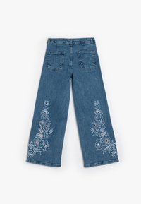 Pantalones vaqueros de pierna ancha en azul medio con bordados florales en blanco, rojo y verde en ambas piernas. Incluye dos bolsillos traseros.