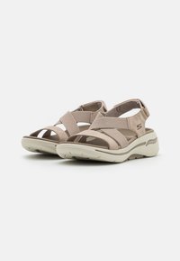 Beige sportieve sandalen met kruisbanden, elastisch materiaal, gevoerde binnenzool en een lichtbeige rubberen zool met een gestructureerde grip.