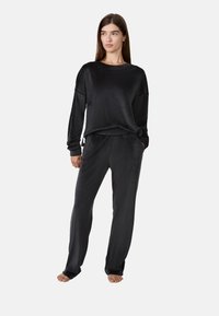 Zwart velours loungewearset met een relaxte lange mouwen top en bijpassende broeken met een elastische tailleband en zijzakken.