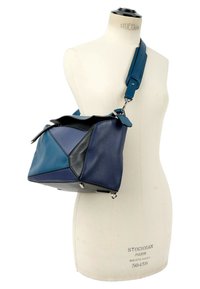 Sac à main en cuir bleu et noir à motifs géométriques avec une large bandoulière réglable, exposé sur un mannequin torse blanc.