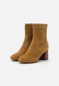 Brune suédé ankelstøvler med spids tå, elastiske sidepaneler og en stablet træhæl. Glat tekstur med subtile syninger.