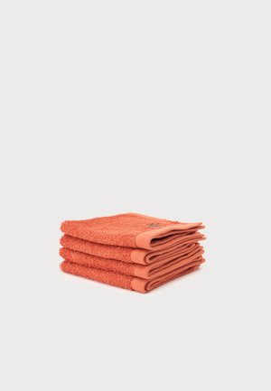 Pile de trois serviettes pliées de couleur corail avec un tissu texturé sur un fond gris clair.