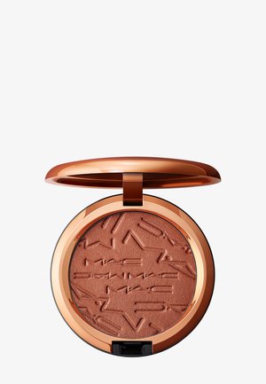 Poudre compacte bronzée avec motif étoile et texte en relief, logée dans un boîtier en or rose brillant avec couvercle ouvert.
