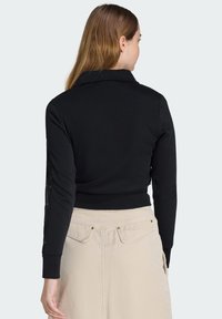 Pull court noir à manches longues, avec un col et des panneaux latéraux texturés. Associé à une jupe beige clair, ornée de détails à boutons.