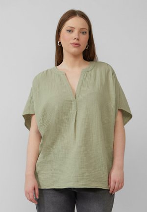 Haut vert clair à manches courtes avec un col en V, en tissu doux et texturé, et coupe décontractée. Présente un léger motif froissé.