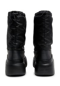Botas negras de altura a los tobillos con un eje de textil estampado, acabado mate suave y suelas de goma negra sólida. Logo registrado en la parte trasera.