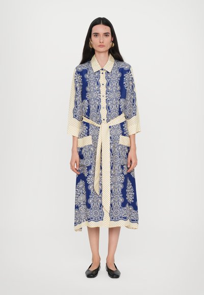 Long dress featuring a navy blue and cream floral pattern with polka dots, a collared neckline, button front, and side pockets.