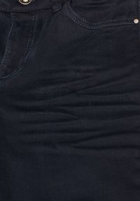 Jeans de mezclilla en azul oscuro con una textura suave, ligeras desgastadas, un diseño clásico de cinco bolsillos y cierre de botón de metal.