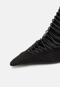 Botine negre din suede, cu vârf ascuțit, având un design cu șireturi și detalii de șireturi verticale pe tijă. Textură netedă.