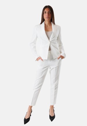 Completo bianco su misura composto da un blazer slim-fit con un solo bottone, abbinato a pantaloni tapered. Scarpe con tacco nere completano l'outfit.