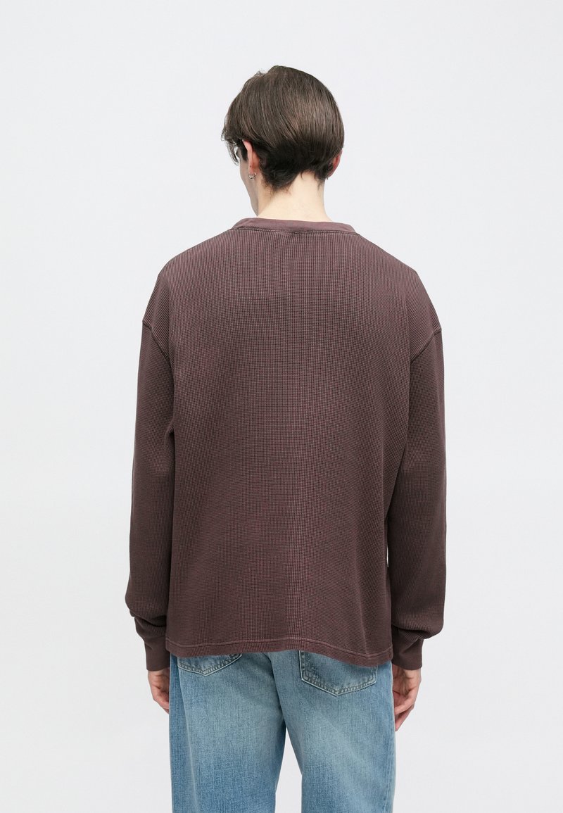 Brun tekstureret langærmet skjorte med løs pasform og rund hals, kombineret med lyseblå jeans.