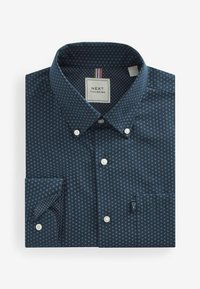 Chemise bleu foncé à manches longues pliée, avec un motif géométrique bleu clair, des boutons blancs et une étiquette "NEXT Tailoring" à l’intérieur du col.