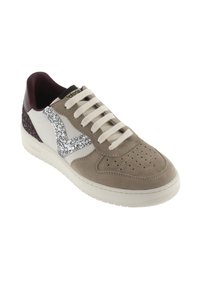 Sneaker in suede beige con dettagli in pelle bianca, un logo argentato scintillante e tacco color bordeaux. Presenta dettagli perforati e lacci color crema.