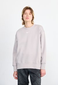 Lys grå hettegenser med rund hals og ribbestrikkede mansjetter, med en liten hvit Nike-logo på brystet. Teksturert stoff.