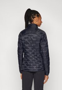 Veste matelassée navy avec une silhouette ajustée, un léger éclat, une texture matelassée, un col haut et des poignets élastiques, conçue pour la chaleur et le confort.