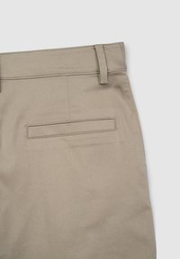 Pantalon beige à la texture lisse, doté d'une seule poche arrière et de passants de ceinture, partiellement visibles depuis la taille.