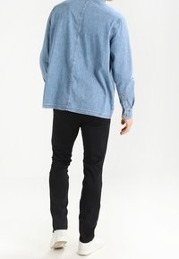 Světle modrá denimová košile s uvolněným střihem, černé úzké kalhoty a bílé tenisky. Bavlněný materiál, žádné viditelné vzory nebo akcenty.