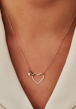Goldene Halskette mit einem herzförmigen Anhänger und einem kleinen Charm, an einer zarten Kette aufgehängt. Das Herz hat eine glatte, polierte Oberfläche.