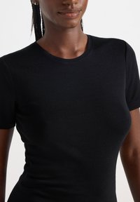 Svart kortärmad t-shirt i mjukt tyg med rund halsringning. Passformen är kroppsnära och framhäver en slät yta och minimala sömmar.