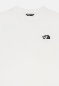 Balta kokvilnas T-kreklu ar melnu izšūtu logo "The North Face" kreisajā krūtī. Klasisks apaļš kakla izgriezums.