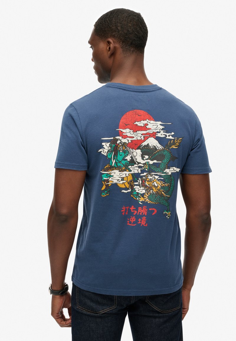 T-shirt en coton bleu marine avec un graphisme au dos représentant des guerriers, un dragon et une montagne sous un soleil rouge, avec des détails colorés et du texte.