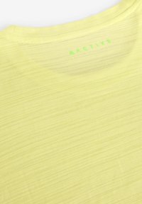 Heled kollane spordisärk, millel on tekstureeritud muster, ümmargune kaelus ja rohelise "ACTIVE" logo kaela tagaosal.