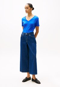 Blauwe V-hals T-shirt, wijde blauwe jeans met een hoge taille en zwarte instap schoenen. Glad textuur, minimalistisch ontwerp en geen zichtbare patronen.