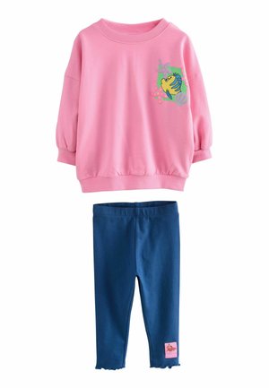 Rosa Sweatshirt mit Puffärmeln und einem Fischdesign, kombiniert mit marineblauen Leggings mit einem gewellten Saum und einem pinken Etikett an der Seite.