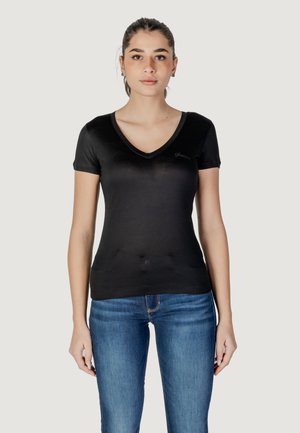 T-shirt nera a maniche corte con scollatura a V, realizzata in tessuto morbido, con un logo discreto sul lato sinistro, abbinata a jeans blu.