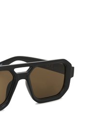 Lunettes de soleil noires angulaires avec verres marron, dotées d'une monture épaisse et d'accents découpés sur le pont supérieur. Texture lisse partout.
