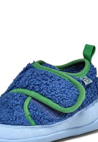 Blauer, flauschiger Velcro-Schuh mit grünen Akzenten, strukturiertem Obermaterial und einer glatten, hellblauen Sohle. Verfügt über eine Fersenschlaufe für ein einfaches Anziehen.