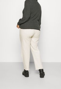 Szary sweter dziany, beżowe spodnie o szerokich nogawkach z postrzępionymi brzegami oraz czarne botki za kostkę. Skupienie na fakturze i casualowych elementach designu.