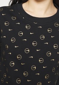 Czarna bluza z kapturem z powtarzającym się wzorem złotych logo Nike i grafik koszykarskich, z okrągłym dekoltem i teksturowaną tkaniną.